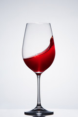 Wave of the romantic drink red wine on the pure wineglass standing against light background with reflection.