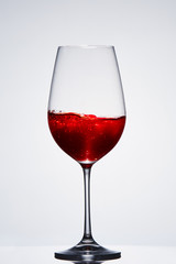 Fragile elegant wineglass of red wine standing against light background.