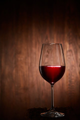 Half-full fragile wineglass of red wine standing on a wooden background.