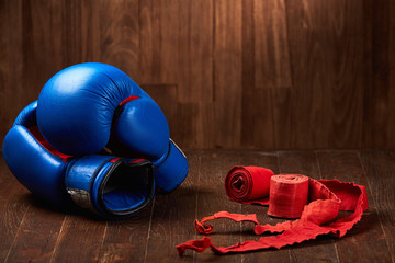 Pair of blue boxing gloves with two rolls of hand bandage on wooden background.