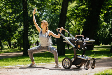 Beautiful young sporty woman with baby stroller workout outside in summer nature park. Sport, maternity and healthy lifestyle concept.