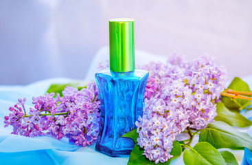 Blue glass perfume bottle with drops of water on a white box and  beautiful  fresh lilac flowers...