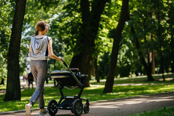 Fototapeta na wymiar Beautiful young sporty mother jogger with baby stroller running outside in summer nature