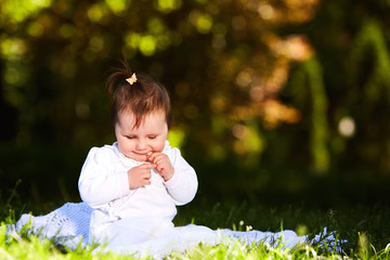 Adorable cute baby girl sitting on green meadow and eating the pastry.