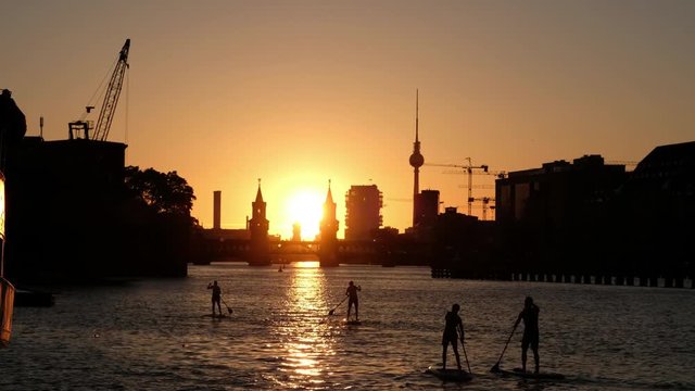 group of paddle board / stand up paddler on river spree in Berlin - Oberbaum Bridge, Tv Tower and sunset sky background