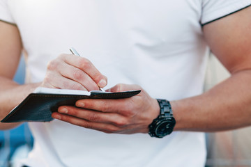 Cheerful young man in white T-shirt writing his notebook on parking