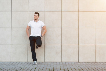Fototapeta na wymiar Portrait of Young Muscular Man in White T-shirt Standing Near the Wall