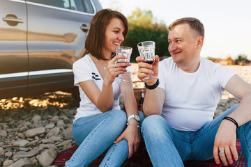 Portrait of happy young adult couple on roadtrip. Man sitting on plaid with woman. Outdoor picnic concept.