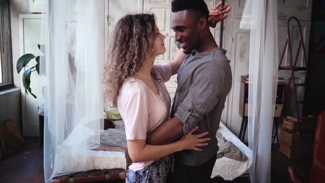 Beautiful multiethnic couple in pajamas dancing together and smiling. Man and woman having fun. Slow motion.