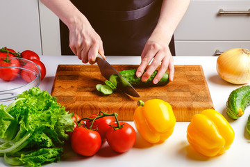 Woman cutting fresh cucumber on wooden board ingredients for salad