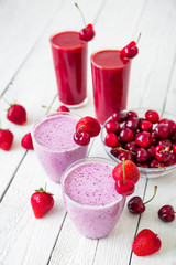 Cherry and strawberry milkshake and tasty summer berries on white wooden table. Fresh natural smoothie