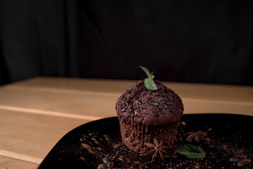 Chocolate muffin in a black plate with some mint and  anis star on a black background