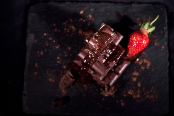 Strawberry lying behind of a chocolate pyramid on a blacj background