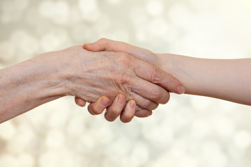 Handshake between an old person with a wrinkled hand and a kid, on a beige bokeh  light background.