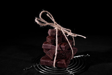 A stack of black pore chocolate tied with twine thread from twine on a black background