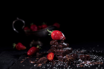 Strawberry lying on a pyramid of chocolate with sliced other strawberries and old silver vase
