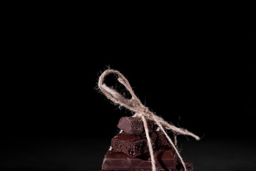 A stack of black pore chocolate tied with twine thread from twine on a black background