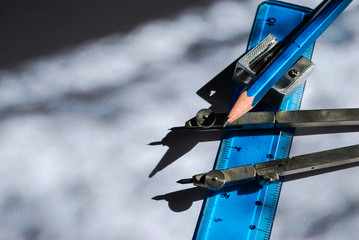 A compass, ruler, crayon and metal sharpener between the shadows and lights