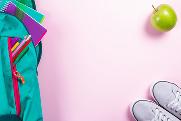 Backpack with school stationery on pink background