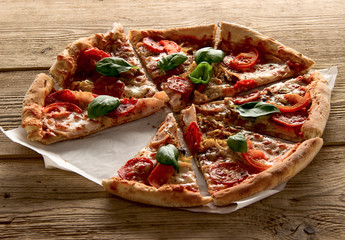 Hot and delicious pizza with salami tomatoes cheese and mushrooms ready to eat  on a wooden background.