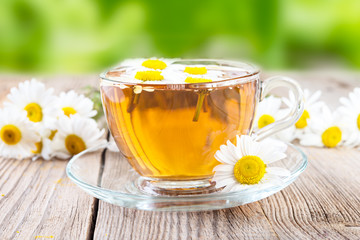 cup of camomile tea and  camomile flowers on wooden background