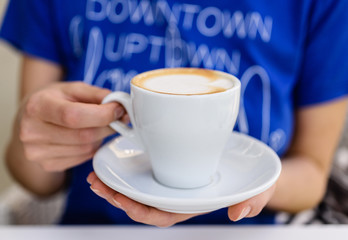 Closeup of woman hands with cappuccino coffee cup in a cafe
