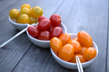 Cherry tomatoes in a snack bowl on wooden background.