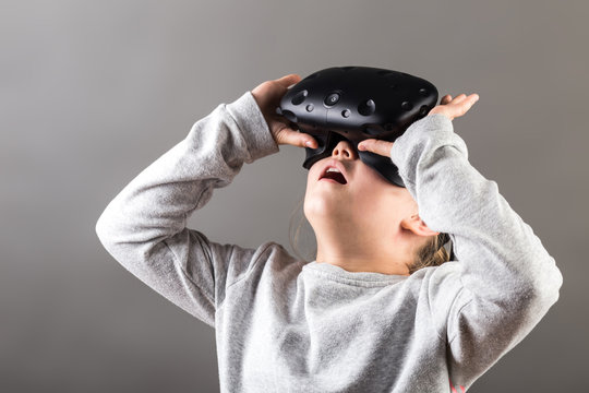 lifestyle shot of an amazed little kid using a virtual reality goggles with mouth open shocked seated on wooden floor in the living room at home. family activity concept.
