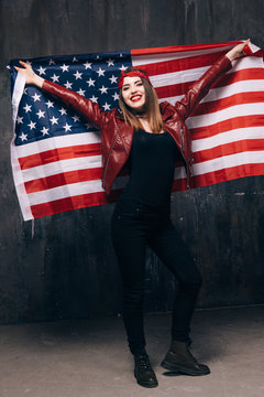 Happy smiling girl with USA flag behind the back on dark background. American patriot, national event celebration, pride, us citizen concept