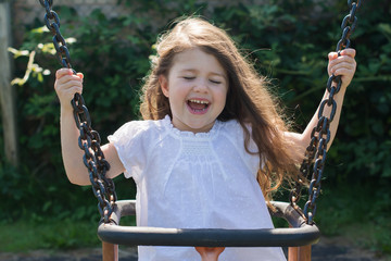 Little girl in a white top on a swing in the park, selective focus