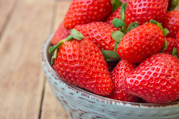 Ripe organic strawberries in blue ceramic bowl on plank wood background, close up, healthy food, cleansing concept