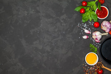 Cooking background. Ingredients and spices for cooking dinner: tomatoes, greens, salt, pepper, garlic. With a frying pan, on a black concrete table. Top view