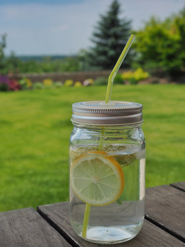Elder syrup, water, slace of lemon and elder flower in glass with green straw.