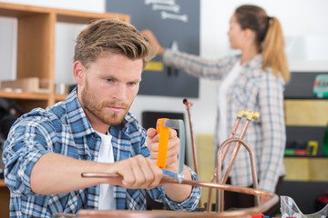 Tradesman cutting copper pipe with hacksaw