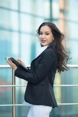 Beautiful young girl in a black jacket with a folder and pen in hand on the background of a glass building