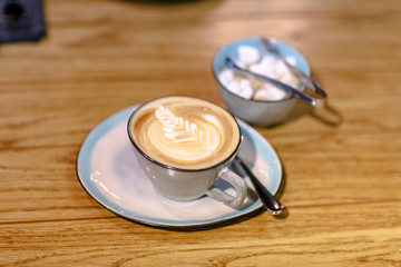 Cup of cappuccino with a pattern and a sugar bowl with brown and white sugar are on the table