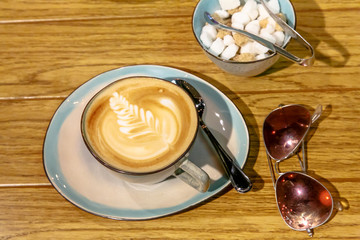 Cup of cappuccino with a pattern and a sugar bowl with brown and white sugar are on the table
