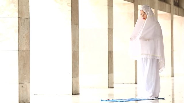 Religious muslim woman doing praying in the mosque with full poses on two rakat: standing, bowing, prostration, sitting, and greeting