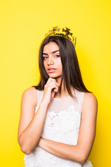 Beautiful young woman wearing crown and nice dress on yellow background