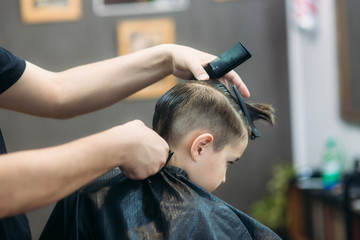 Little boy on a haircut in the barber sits on a chair.