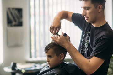 Little boy on a haircut in the barber sits on a chair.