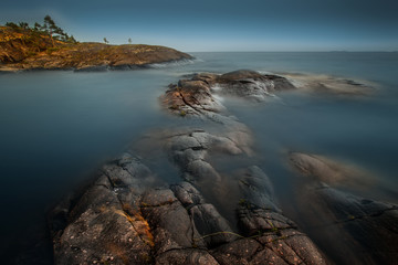 Fototapeta na wymiar Rocky shore at night. Water on long exposure. Northern nature. Wild places. Strait between the rocks.