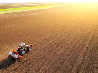  Aerial shot of a farmer seeding, sowing crops at field. Sowing is the process of planting seeds in the ground as part of the early spring time agricultural activities. © oticki