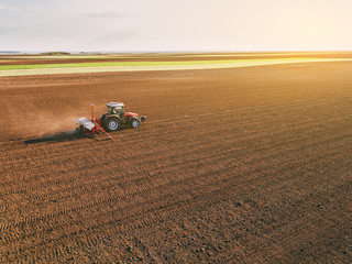 Aerial shot of a farmer seeding, sowing crops at field. Sowing is the process of planting seeds in...