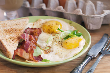 American breakfast with sunny side up eggs, bacon, toast, coffee, green salad, wood background