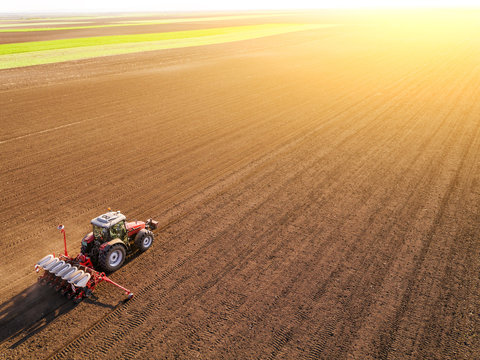 Fototapeta Aerial shot of a farmer seeding, sowing crops at field. Sowing is the process of planting seeds in the ground as part of the early spring time agricultural activities.
