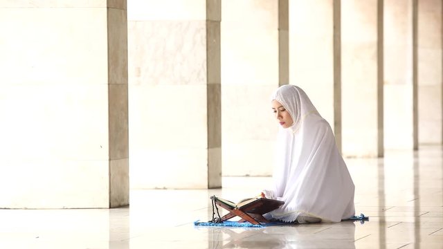 Video footage of a young religious muslim woman reading Quran in the mosque while wearing prayer veil
