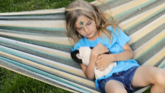 Child blond girl sitting or lying in a hammock and holding her guinea pig pet animal.