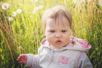 Baby girl sitting in the grass on a background of white dandelions.