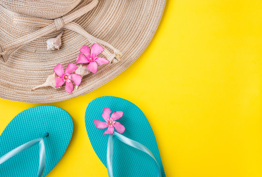 Women's straw hat, pink tropical flowers, blue slippers, sea shells, on yellow background, beach vacation, seaside, fashion, top view